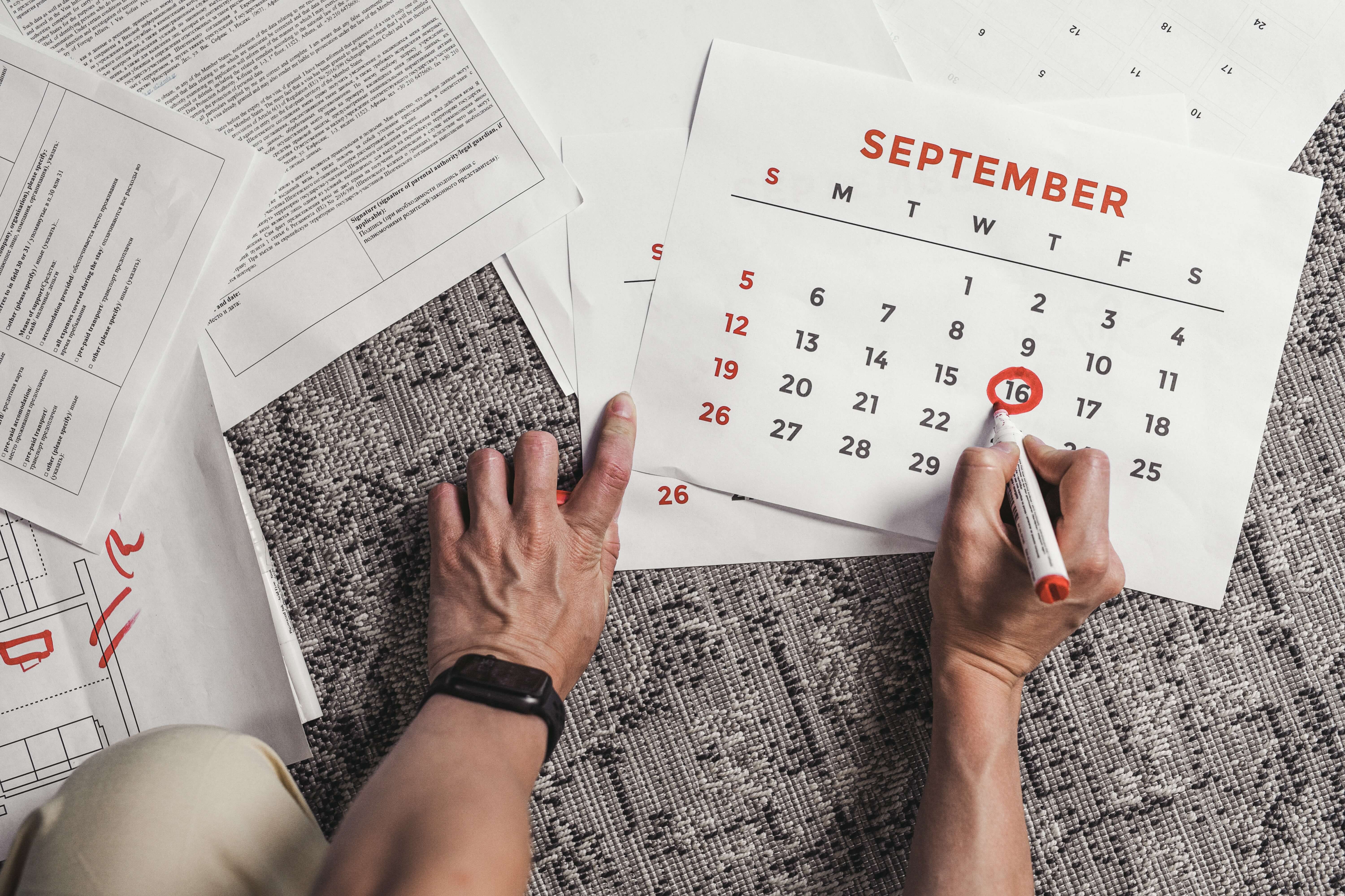 An individual circling a date on a calendar of September in a bright red marker